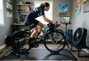 Indoor bike trainer positioned on a thick rubber mat in a home training room with a fan and water bottle nearby