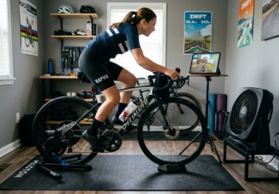 Indoor bike trainer positioned on a thick rubber mat in a home training room with a fan and water bottle nearby